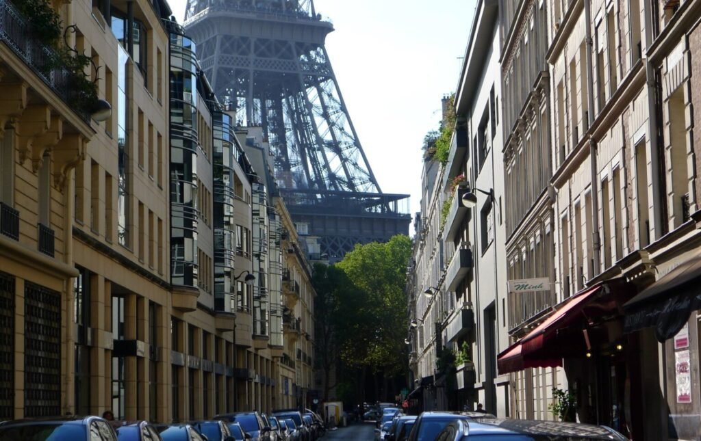 A narrow Parisian street lined with classic buildings, leading towards the base of the Eiffel Tower in the background."