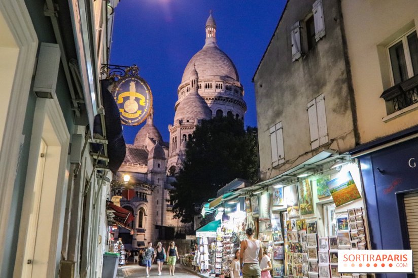 A charming evening scene in Montmartre, Paris, with the illuminated Sacré-Cœur Basilica in the background and a lively street with souvenir shops and pedestrians in the foreground.