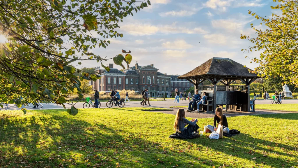 People relaxing on the grass in Hyde Park with Kensington Palace in the background