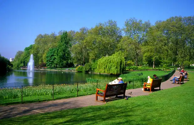 Green park with lake, fountain, benches, and people relaxing